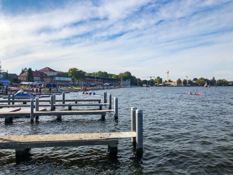 The photo shows the regatta course in Grünau. You can see canoes in the water and the boat docks.