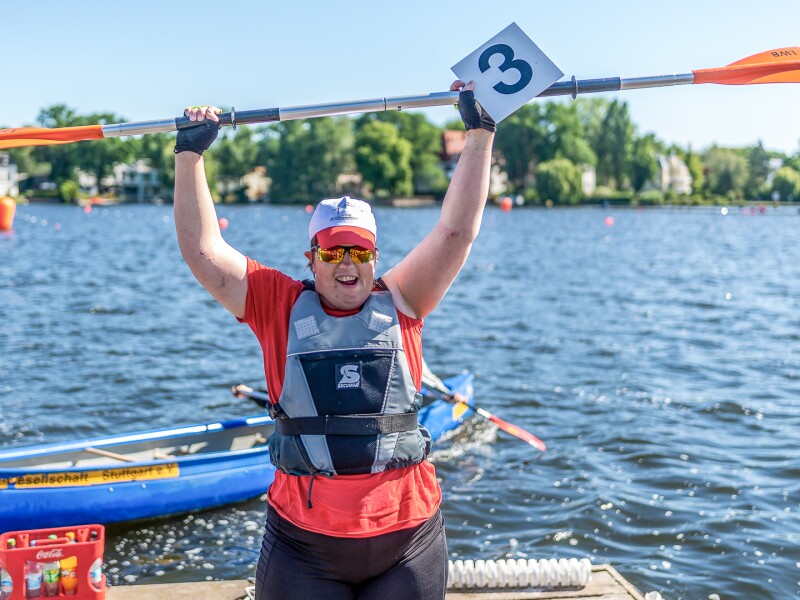 The photo shows kayakist Juliana Rößler after winning the kayaking race during the Special Olympics National Games Berlin 2022, holding her paddle above her head in jubilation.