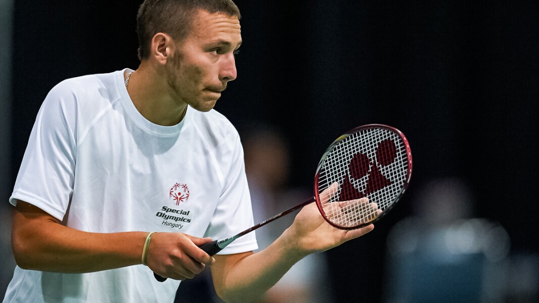 Auf dem Foto ist ein Athlet zu sehen, der konzentriert schaut und einen Badminton-Schläger in der Hand hält.