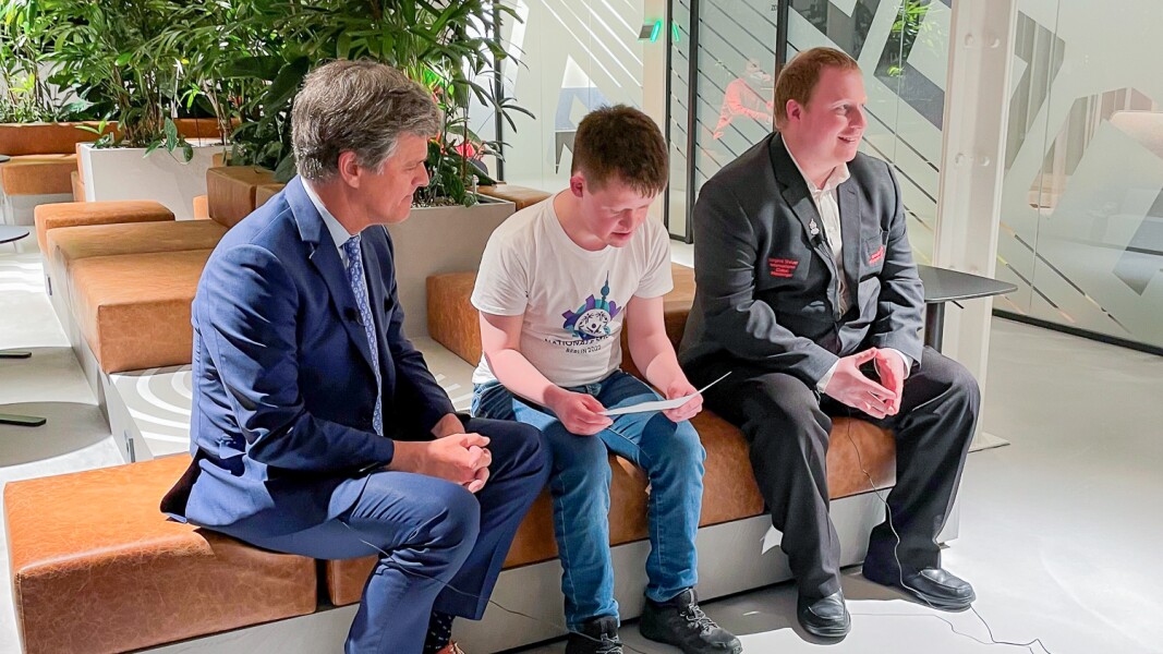 Auf dem Foto sind Timothy Shriver, Arthur Hackenthal und Ian Harper zu sehen, die gerade ein Interview führen und sichtlich Spaß dabei haben.