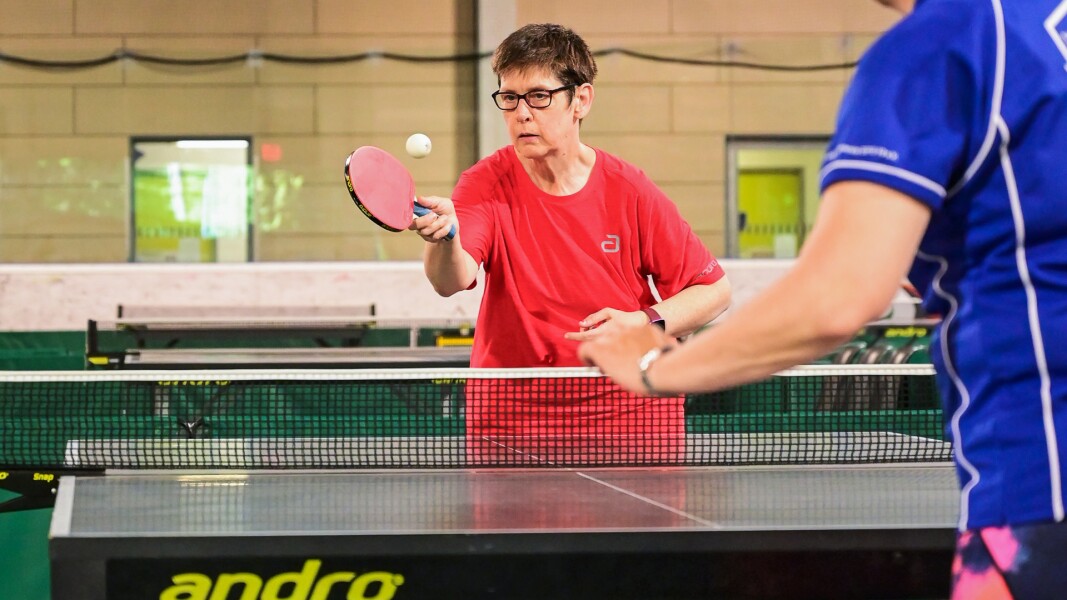 The photo shows a table tennis match. The athlete is looking concentrated while looking at the ball.