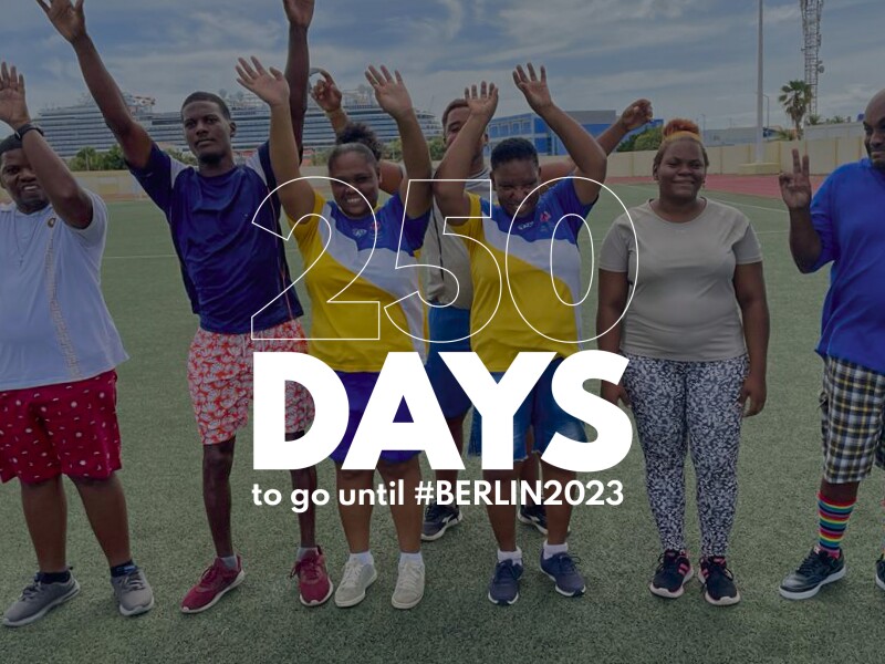 The graphic says "250 days to go until #Berlin2023". In the background is a photo of several people cheering.