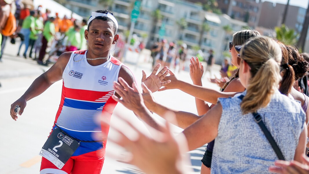 Das Foto zeigt einen Sportler beim Triathlon. Er rennt und klatscht mit den Zuschauer*innen ab.