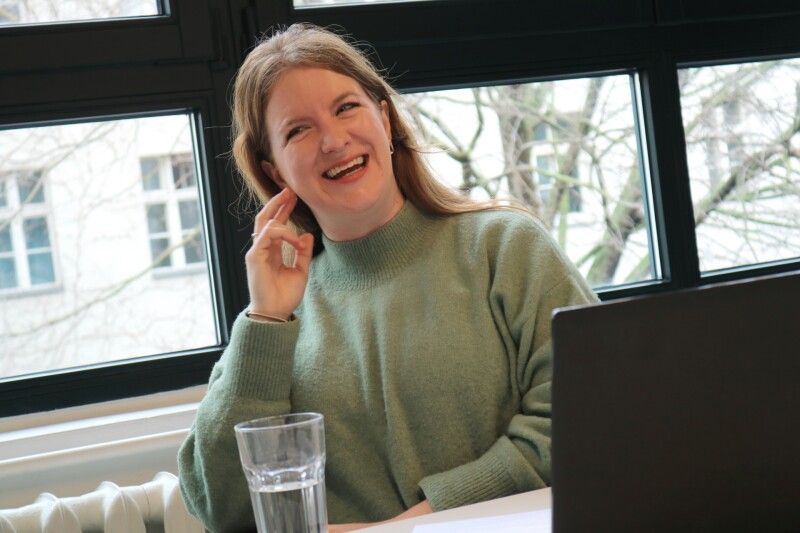 The photo shows our employee Georgia Royes during the interview on the topic "Fans in the Stands". She laughs happily and looks in the direction of the interview partner.