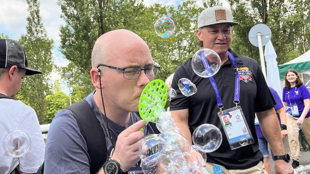 The photo shows two men in the Activity Zone. One of the men is blowing big soap bubbles.
