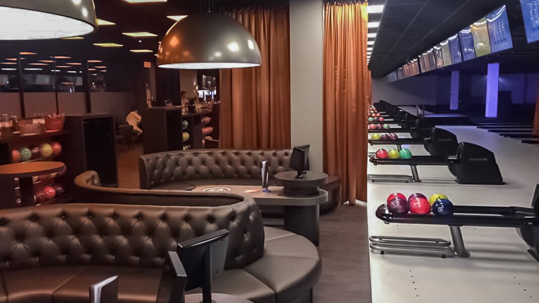 Das Foto zeigt einen Sitzbereich mit Monitoren und mehrere Bowlingbahnen im Anschnitt in einem Berliner Bowlingcenter.