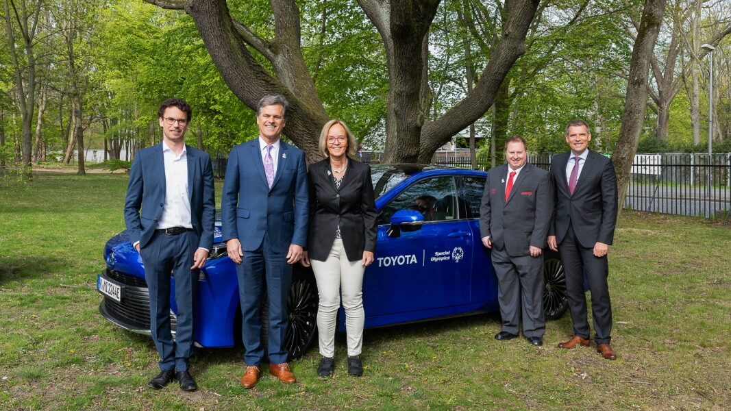 The photo shows five people standing in front of a car and smiling. The car is a Toyota because Toyota sponsors the Special Olympics events in Berlin.