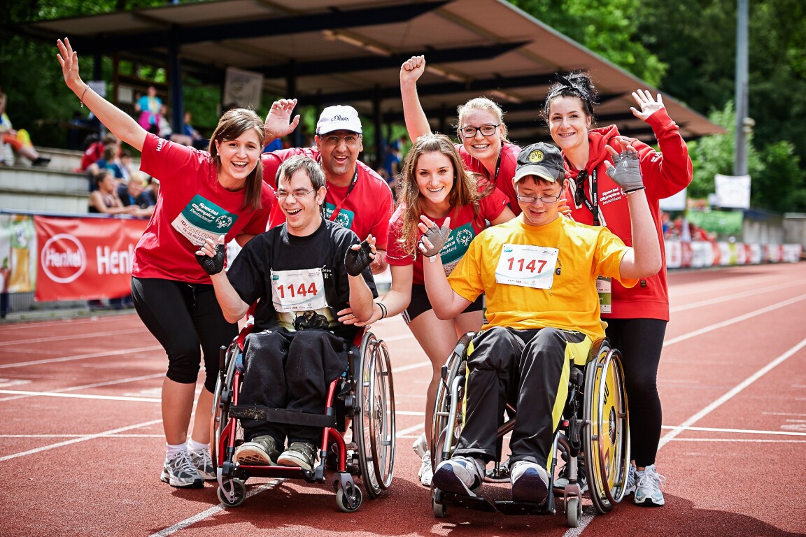 Das Bild zeigt eine Gruppe von Volunteers die mit zwei Athleten feiert.