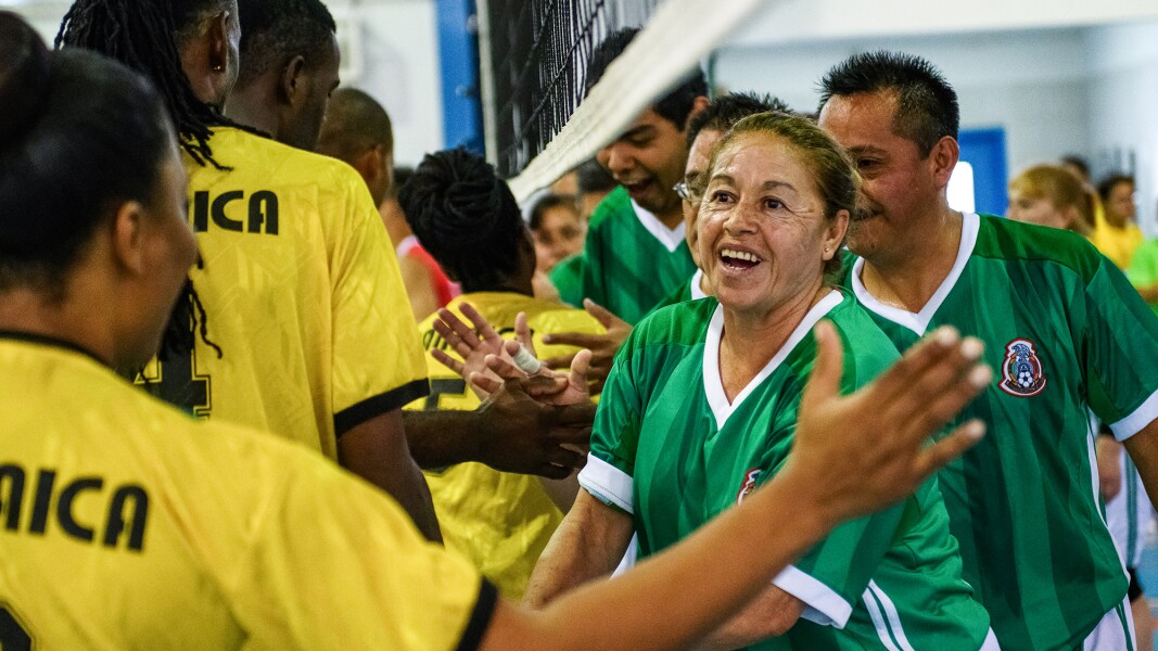 Auf dem Foto sind zwei Mannschaften beim Volleyball zu sehen, die gerade freudig unter dem Netz gegenseitig abklatschen.