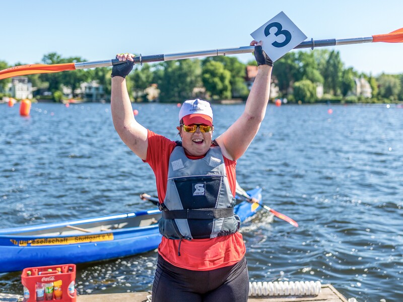 Das Foto zeigt die Kanutin Juliana Rößler nach ihrem Gewinn im Kanurennen während der Special Olympics Nationalen Spiele Berlin 2022. So hält jubelnd ihr Paddel über dem Kopf hoch.
