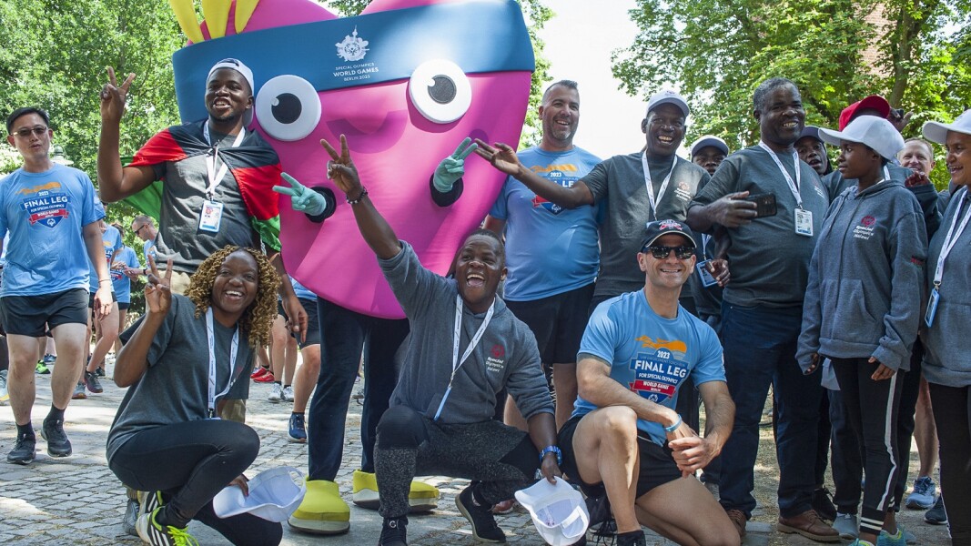 Das Foto zeigt eine Szene während des Law Enforcement Torch Run. Viele Menschen und das Maskottchen Unity jubeln in Richtung Kamera.