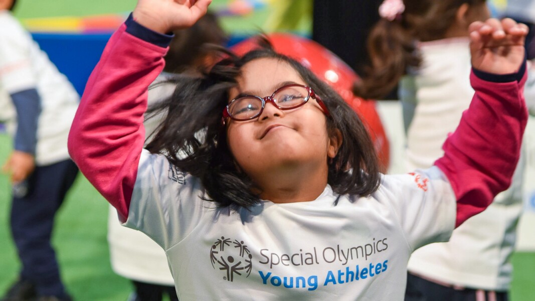 Das Foto zeigt ein Mädchen, dass die Arme in die Höhe gerissen hat und sich über etwas freut. Das Bild entstand im Rahmen des Young Athletes Programms von Special Olympics.