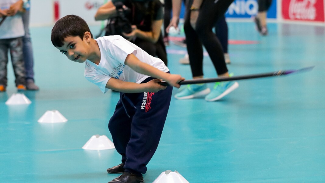 Auf dem Foto ist ein kleiner Junge, der gerade einen Ball mit seinem Hockeyschläger geschlagen hat. Es ist im Rahmen des Young Athletes Programms entstanden.