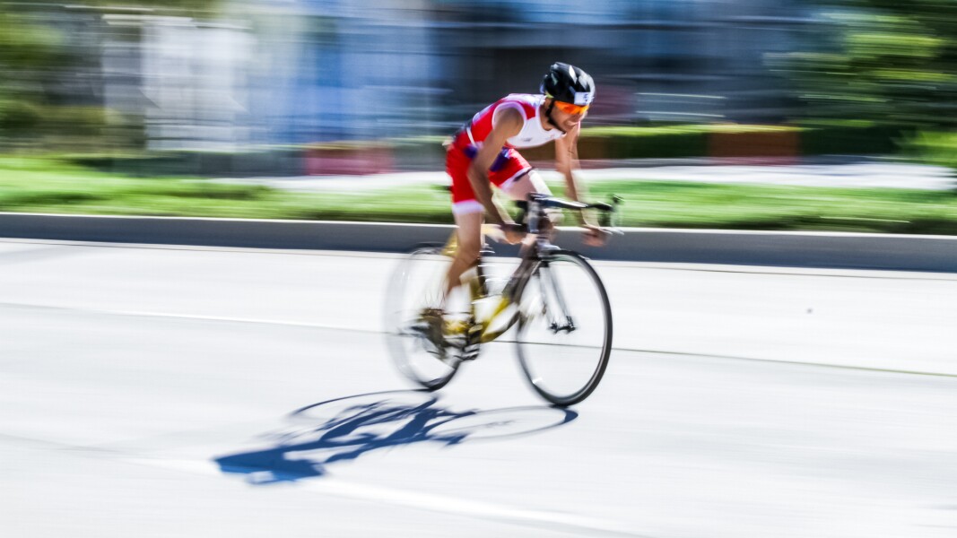 Das Foto zeigt einen schnell fahrenden Radfahrer. Es ist durch die Geschwindigkeit leicht verzerrt und gibt damit einen sehr dynamischen Eindruck.