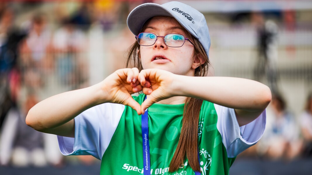Auf dem Bild sieht man eine Athletin, die mit ihren Händen ein Herz formt.