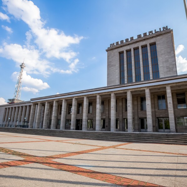 The photo shows a paved forecourt and a building with columns on which Messe Berlin stands.