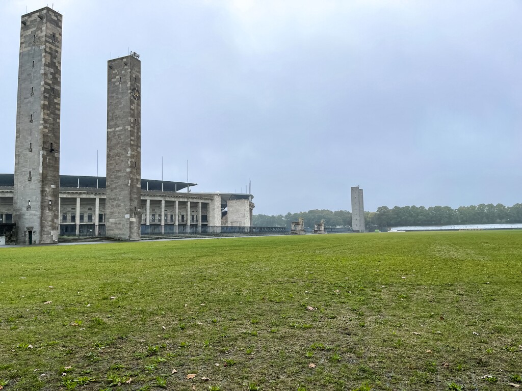 Das Foto zeigt eine Rasenfläche im Vordergrund und zwei große Säulen, sowie das Berliner Olympiastadion im Anschnitt.