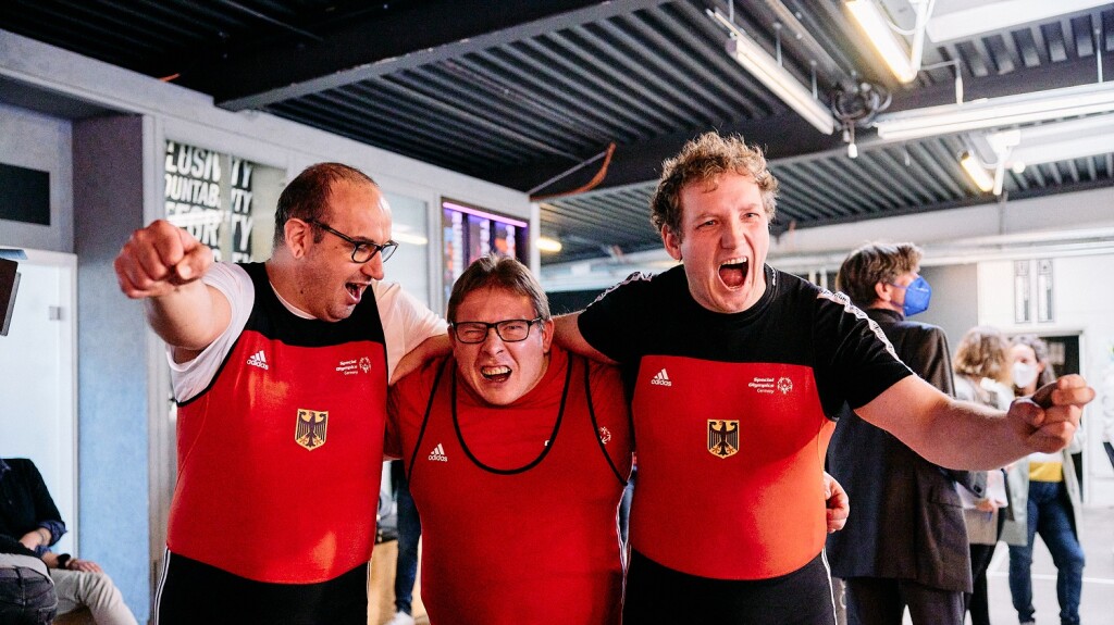 Auf dem Foto jubeln drei Special Olympcis Deutschland Athleten in die Kamera. Sie haben gerade erfahren, dass sie für das Team SOD bei den Weltspielen im Kraftdreikampf antreten dürfen.