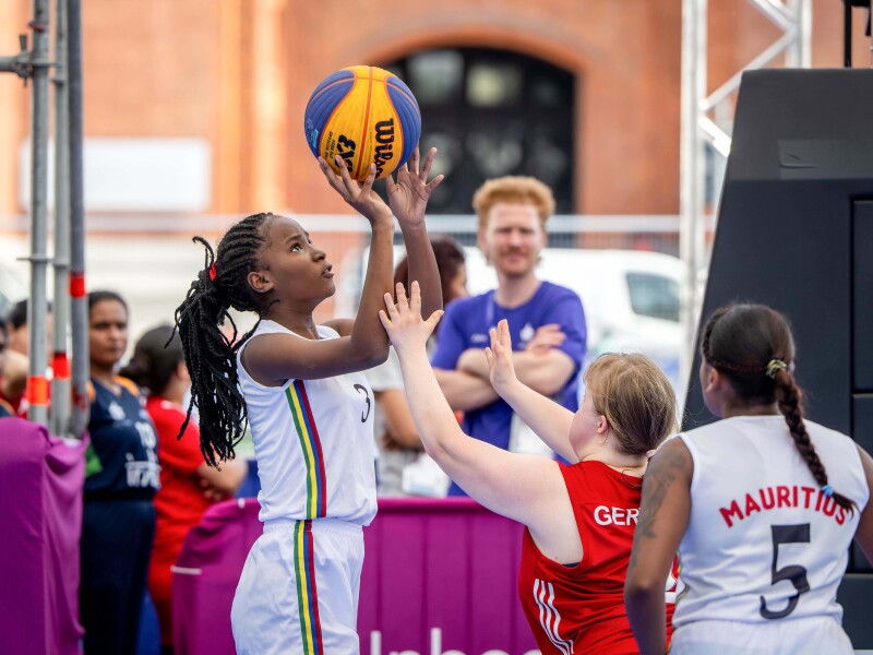 The Mauritian female athletes wearing the white jerseys is trying to score while the German female athlete wearing the red jersey is trying to block the shot
