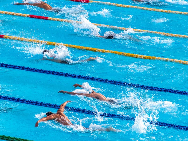 Das Foto zeigt mehrere Schwimmbahnen in einer Schwimmhalle und Menschen die schwimmen.