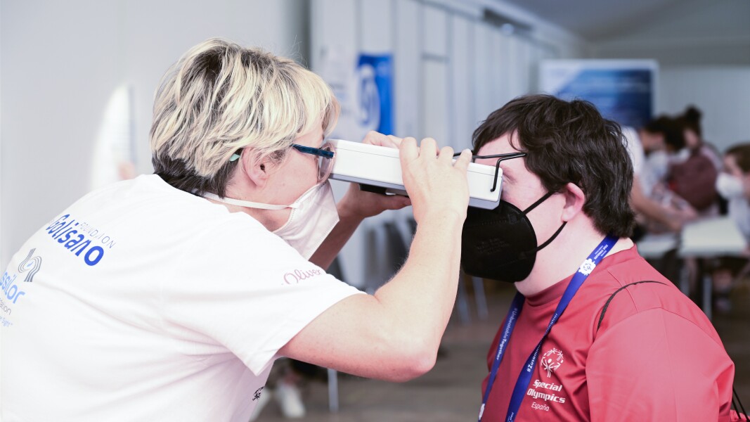 A woman is doing an eye examination with an athlete. She is looking in the eyes of the athlete with the help of a special device.