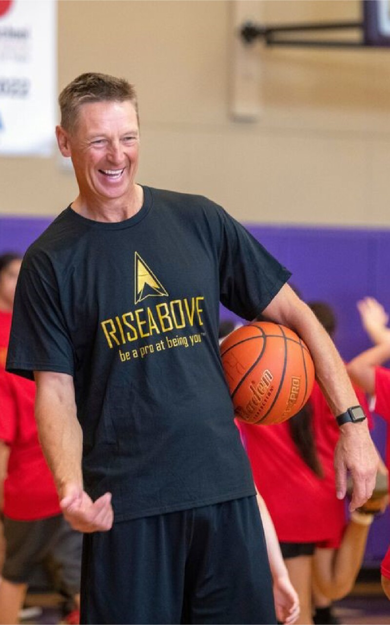 Das Foto zeigt den ehemaligen Basketballer Detlef Schrempf mit einem Basketball unter dem Arm. Er lacht vergnügt.
