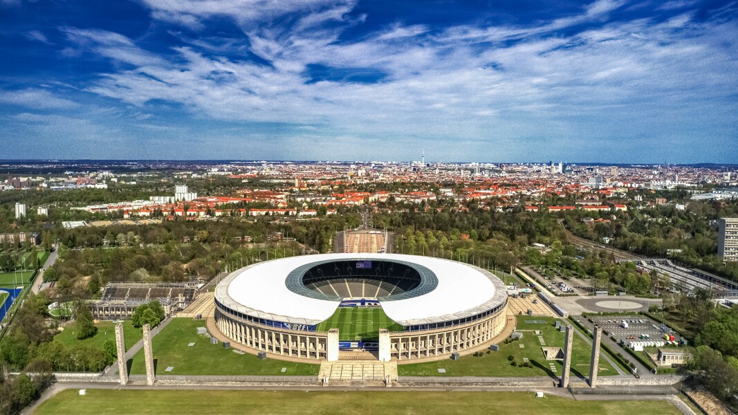Photo shows bird's eye view of Berlin Olympic Stadium and city area behind it.