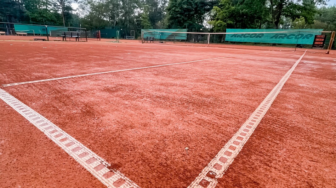 Das Foto zeigt einen roten Tennisplatz im Freien. Der Fokus liegt auf einer Ecke.