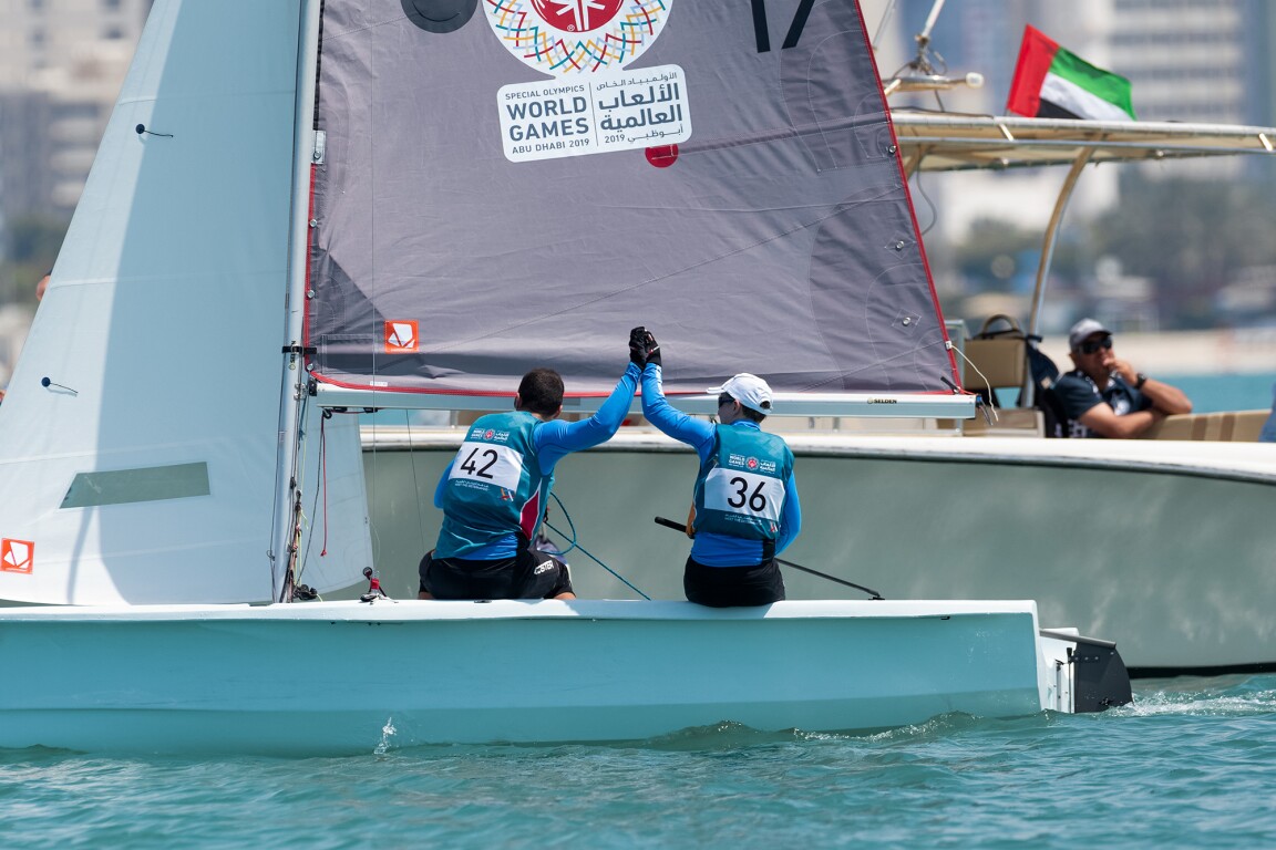 The photo shows two athletes on a sailing boat, who give each other a high five.