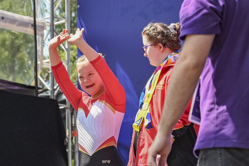 Athletin Annabelle kommt auf das Podium zur Siegerehrung und jubelt in Richtung des Publikums. Dabei hat sie die Arme nach oben zum Jubeln gestreckt.