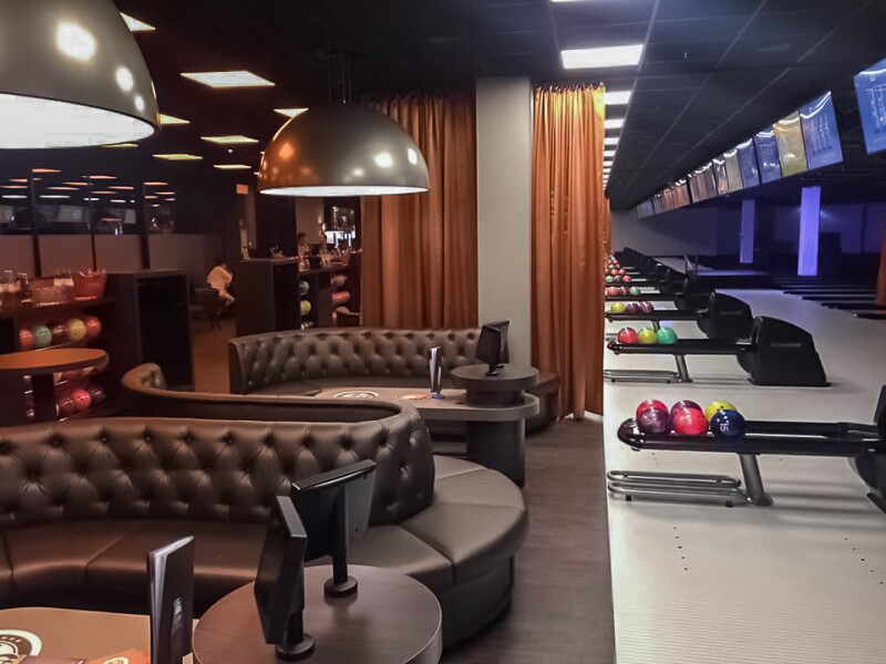 Das Foto zeigt einen Sitzbereich mit Monitoren und mehrere Bowlingbahnen im Anschnitt in einem Berliner Bowlingcenter.