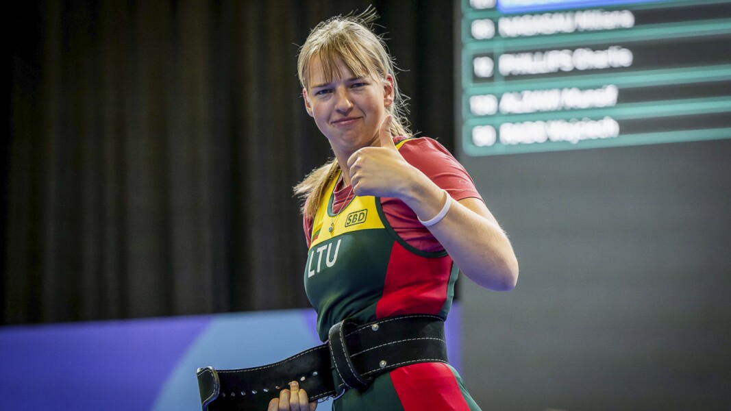 The photo shows an athlete doing powerlifting. She is showing her satisfaction with her thumbs up.