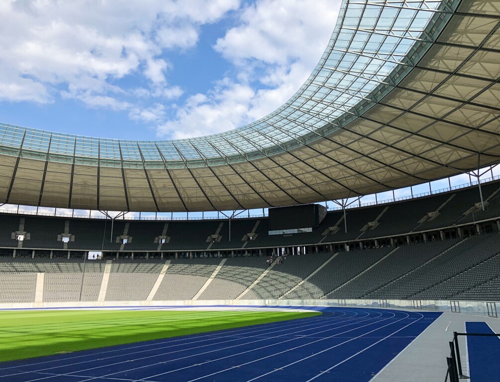 The photo shows a part of the Berlin Olympic Stadium from the inside. There are spectator stands, running tracks and a grassy area in the middle.