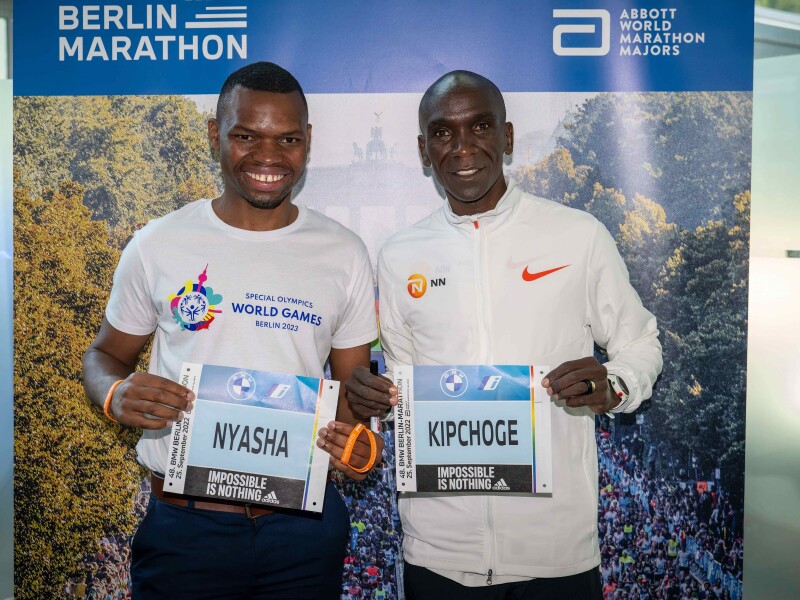 Auf dem Foto halten Special Olympics International Global Messenger und Langstreckenläufer Nyasha Derera und Olympiasieger und Vorbild Eliud Kipchoge ihr jeweiliges Marathon-Namensschild lächelnd in die Kamera.