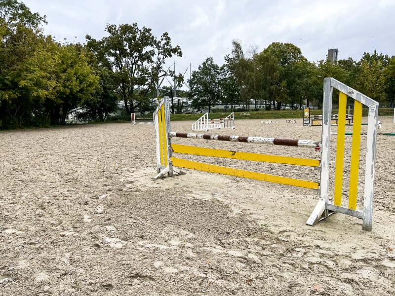 The photo shows an obstacle course for equestrian outdoors. The ground is sandy and the Horst Korber Sports Center is visible in the background.