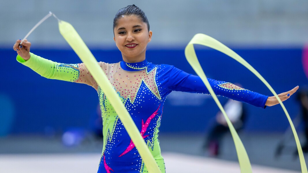 The photo shows a Special Olympics rhythmic gymnastics athlete. She is waving a bright yellow flag and looks very concentrated.