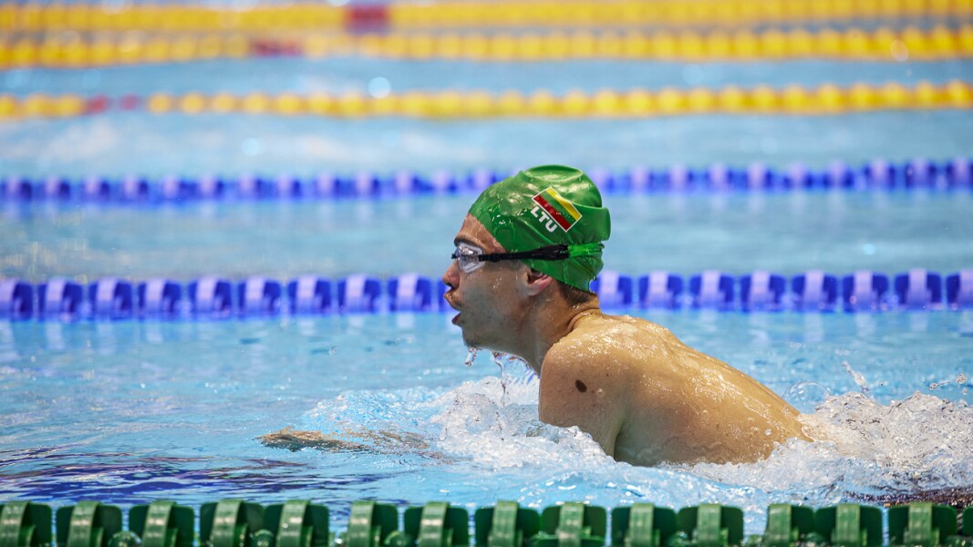 The picture shows a swimmer with green swimming cap from Lithuanian. He is just above water and is setting up for the next stroke in breaststroke.