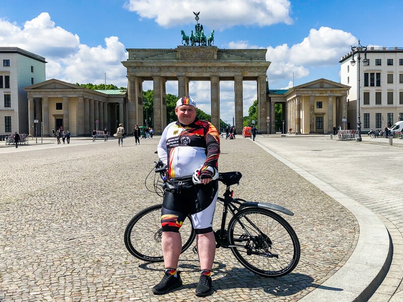 The photo shows Special Olympics Germany athlete Dennis Mellenthin with his bicycle in front of the Brandenburg Gate.