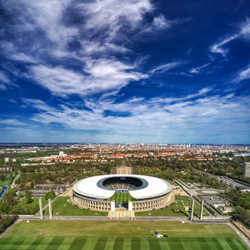 Photo shows bird's eye view of Berlin Olympic Stadium and city area behind it.