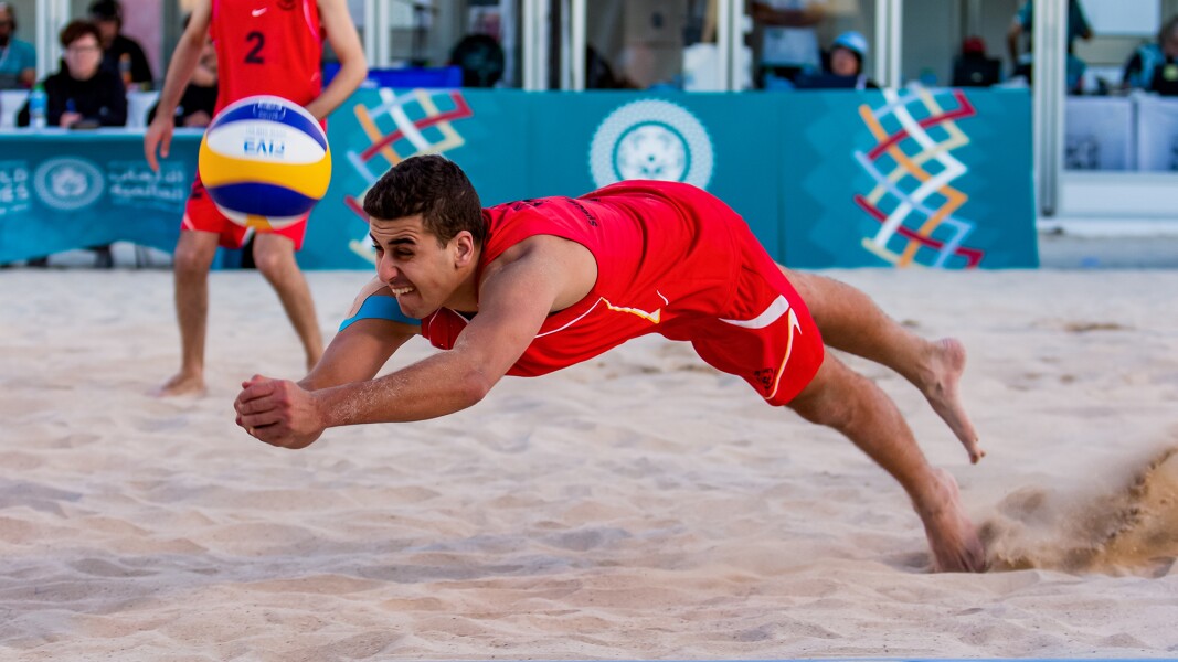 The photo shows a Beach Volleyball players in action, jumping towards the ball.