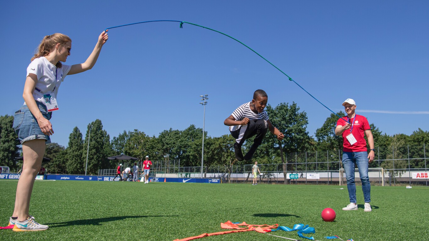 On the photo, there are three people. Two are spinning a rope and the third one, a kid, is jumping with joy in the middle.