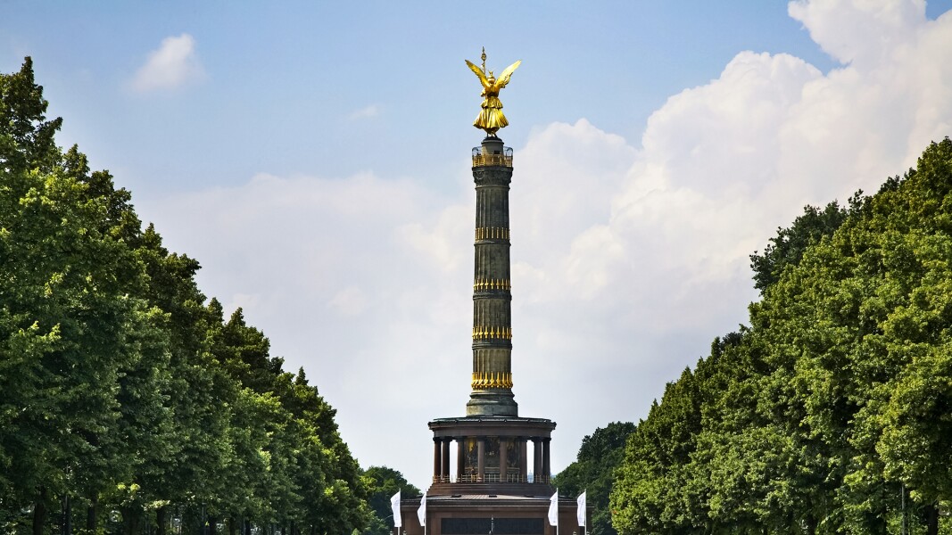 Das Foto zeigt eine Straße mit parkenden Autos und im Mittelpunkt die Siegessäule in Berlin.