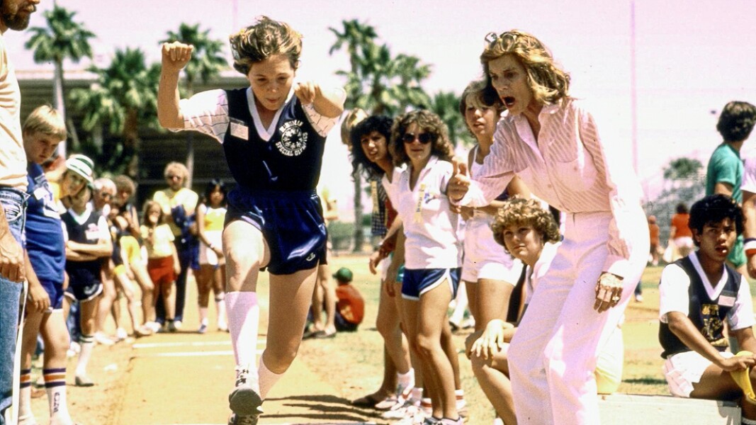 The photo shows Eunice Kennedy Shriver cheering on an athlete doing long jump.