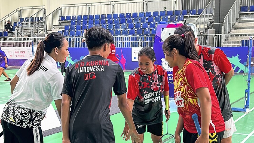 Auf dem Foto sind Athlet*innen beim Badminton zu sehen. Sie fassen sich mit den Händen zu einer Laola zusammen.