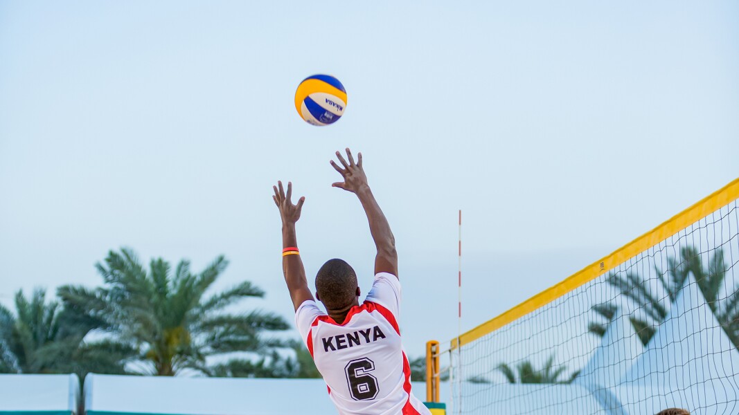 Das Foto zeigt eine Spielszene beim Beachvolleyball. Drei Spieler eines Teams sind in Action, ein Spieler der gegenerischen Mannschaft wartet hinter dem Netz.