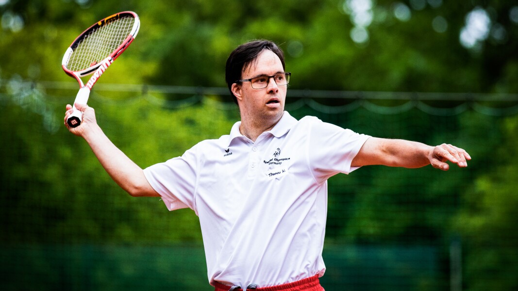 Das Foto zeigt einen Tennisspieler in Action. Er schaut konzentriert und ist in der Bewegung mit seinem Schläger.