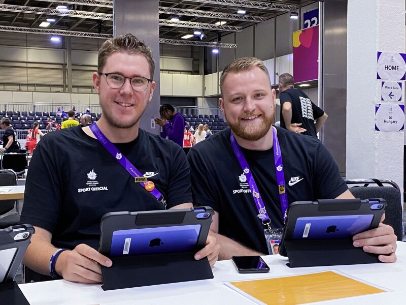 The photo shows the two Unified Observers Felix Beiser and Kilian Wich at work during basketball. Both hold a tablet in their hands and smile friendly.