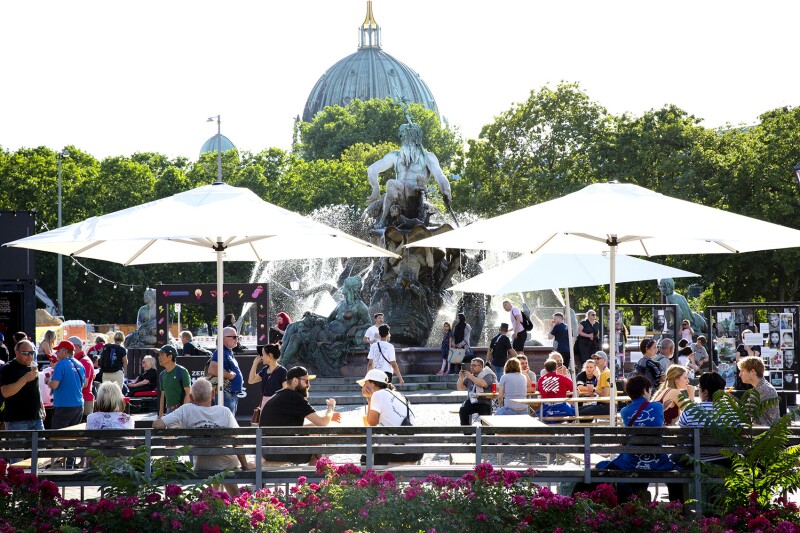 Das Foto zeigt eine Szene des Special Olympics Festivals direkt am berühmten Neptunbrunnen neben dem Alexanderplatz im Herzen Berlins. Viele Menschen schlendern entweder vorbei oder sitzen entspannt auf Bänken.