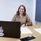 Auf dem Foto ist LOC-Mitarbeiterin Andrea Standecker zu sehen, die an einem Tisch mit Laptop und einigen Unterlagen sitzt. Andrea lächelt entspannt in die Kamera.