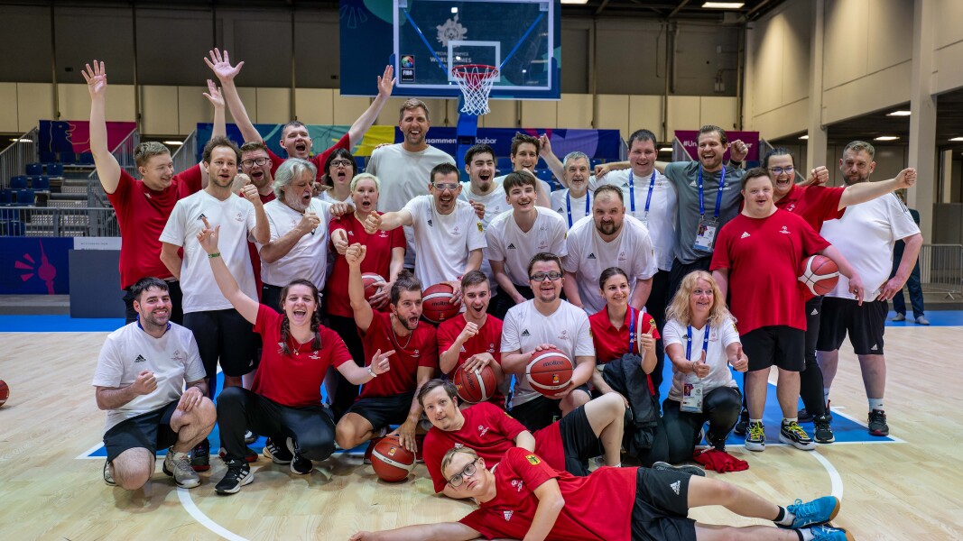 A group picture of the German basketball team cheering with Dirk Nowitzki on the basketball court.